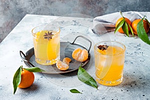 Spicy winter yellow orange cocktail or mocktail with fresh tangerines and anise on grey background.