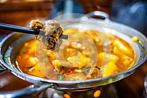 Spicy yak meat in hotpot and fried pig in white plate on wooden table