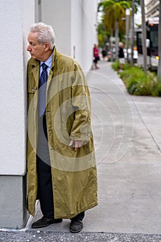 Spies in the city. Old businessman wearing a trenchcoat and spying on his subject in the city