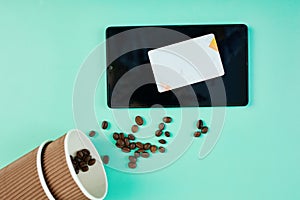 Spilled Coffee Beans Near a Takeaway Cup and Tablet With Credit Card on Teal Background