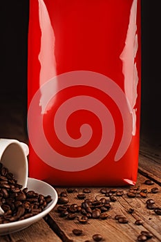 Spilled coffee beans from the white ceramic cup and red package on brown wooden background. Coffee shop, caffeine, roast photo