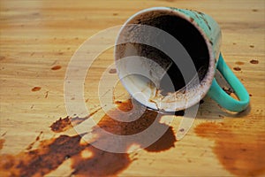 Spilled coffee on parquet floor is a green mug