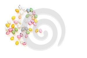 Spilled multicolored quail eggs or small painted chocolate eggs on a white background.