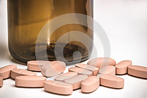 Spilled pink pills from open prescription medication glass bottle