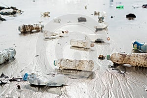 Spilled plastic garbage abandoned on the beach of the big city. Empty used dirty bottles on sand. Environmental pollution