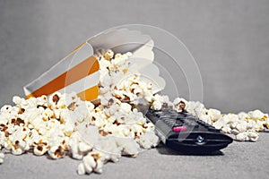 Spilled popcorn and remote control ready for television watching and streaming service on the sofa at home