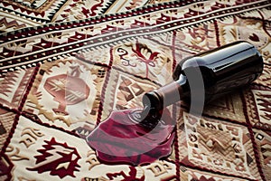 spilled red wine bottle contrasted on a patterned picnic blanket