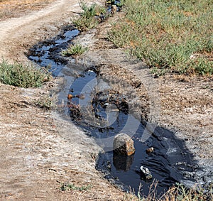 Spilled streams of liquid crude oil flow down drainage ditch into public body of water. Environmental disaster Oil pollution of