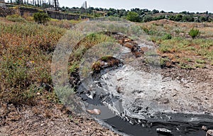 Spilled streams of liquid crude oil flow down drainage ditch into public body of water. Environmental disaster Oil pollution of