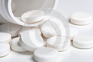 Spilled white pills from open prescription medication plastic white bottle
