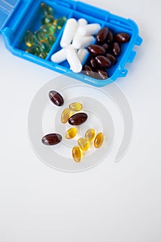 Spilling pills and capsules on a white background close-up together with a container for pills. Top view with copy space. Medicine