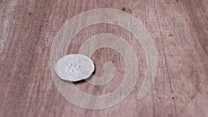 Spin of 5 baht in nonagon shape of ancient Thai money on the wooden floor and stop in reverse of a coin with Garuda form.