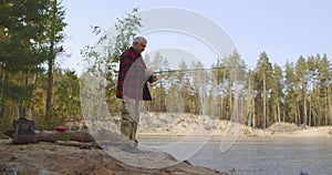 Spin fishing of middle-aged man in forest lake, man is casting rod and rotating reel during angling, relax and enjoy