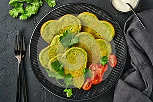 Spinach avocado pancakes in the shape of a heart with greek yogurt sauce and cherry tomatoes on a black plate over dark background