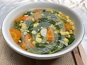 Spinach clear vegetables with carrot pieces served in a white bowl.