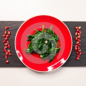 Spinach dish on bright red plate. Vegan healthy food.