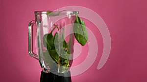 Spinach is falling down to blender on pink background