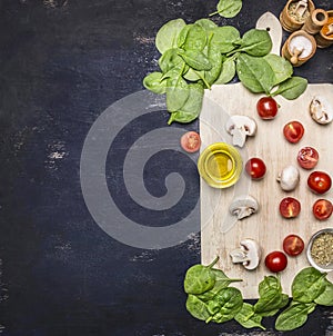 Spinach leaves and sliced mushrooms, laid out on a cutting board with herbs and cherry tomatoes on wooden rustic background top vi