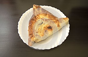 Spinach Manakish on dark wooden background. Spinach triangle pie on white plate