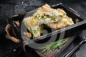 Spinach pie pieces, Spanakopita Greek Pie in wooden tray. Black background. Top view