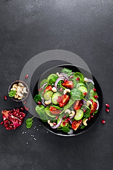 Spinach salad with fresh cucumbers, tomato, onion, pomegranate, sesame seeds and cashew nuts on black background. Healthy vegan fo