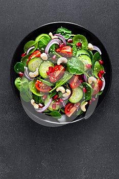 Spinach salad with fresh cucumbers, tomato, onion, pomegranate, sesame seeds and cashew nuts on black background. Healthy vegan fo