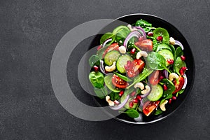 Spinach salad with fresh cucumbers, tomato, onion, pomegranate, sesame seeds and cashew nuts on black background. Healthy vegan fo