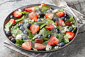 Spinach salad with strawberries, blueberries, cheese and pecans with honey dressing close-up in a plate. Horizontal