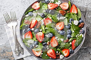 Spinach salad with strawberries, blueberries, cheese and pecans with honey dressing close-up in a plate. Horizontal top view