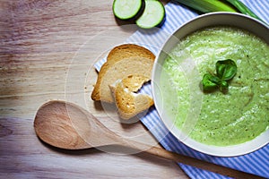 Spinach soup with cream, bread and fresh basil on rustic wood background. Top view