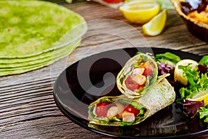 Spinach wrap with meat and vegetables on black plate with green salad