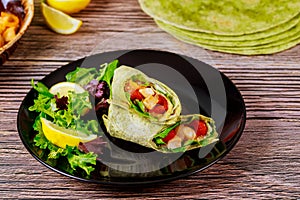 Spinach wrap with meat and vegetables on black plate with green salad