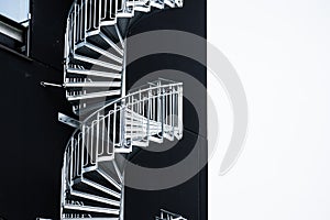 Spiral external emergency stairs by a black building..