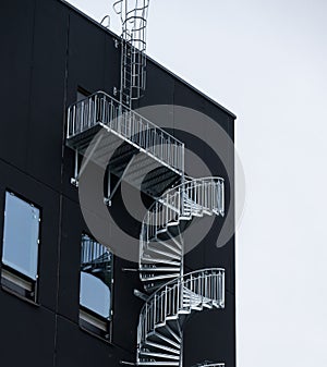 Spiral external emergency stairs by a black building..