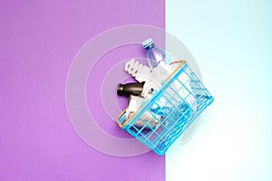 spiral light bulb, can, plastic bottle, packages on a blue toy shopping basket, purple and blue background, copy space