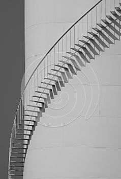 Spiral staircase on oil storage fuel tank with clear sky in vertical frame, black and white style