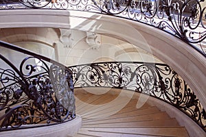 Spiral staircase in Paris with wrought iron railings, shadow play on stone steps. Travel concept