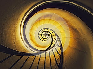 Spiral stairway abstract swirl hypnotising perspective. View downstairs to infinity circular stairs glowing in yellow light