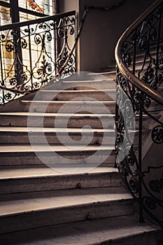 Spiral stone staircase with white granite steps and railings with forged metal patterns