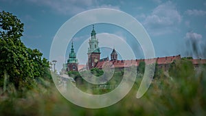 Spire and belltower of Wawel castle in Krakow city, rising up from the green grass up towards the blue sky.. Wide panorama of