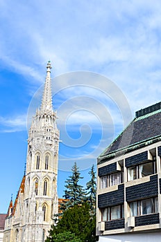 Spire of the Matthias Church in Budapest, Hungary on a vertical photo with adjacent Socialist building. Roman Catholic church