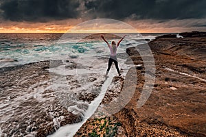 Spirited girl standing over rock crevice as waves wash in