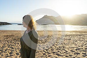 Spiritual adolescent in green dress admire the sunset and the sea town on a hill in Tenerife. Blonde romantic woman look the