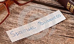 Spiritual blindness. A closeup of a handwritten quote on wooden background with a Holy Bible book and glasses