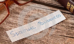Spiritual blindness. A closeup of a handwritten quote on wooden background with a Holy Bible book and glasses photo