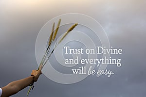 Spiritual inspirational quote - Trust on Divine and everything will be easy. With hand holding bunch of flower plant on blue sky.