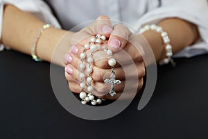 Spiritual prayer to god, with verve or rosary in the hands of a young girl. Black background. Close-up photo