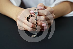 Spiritual prayer to god, with verve or rosary in the hands of a young girl. Black background. Close-up. photo