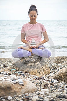 Spiritual yoga woman lotus position on cobblestone with pebble tower harmony relax meditation beach