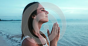 Spiritual young woman praying looking at sky with hope and faith. Religious woman praying at sea in the evening